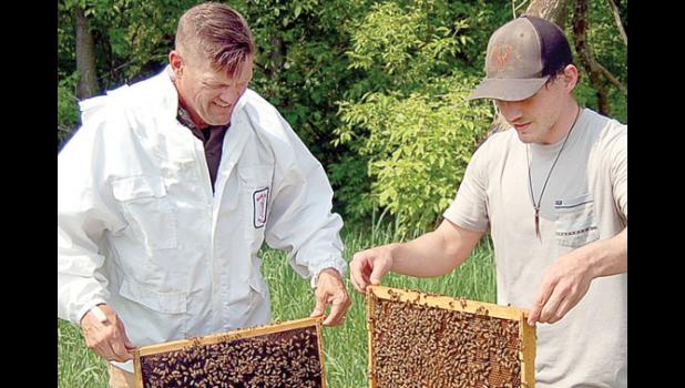 Staff photo Scott Thoma. J.D. Pesch, left, and his son Charlie each held up a frame to show the many bees working to care for the queen while also making honey. Nearly 99 percent of the workers bees are female and are the offspring of the queen.