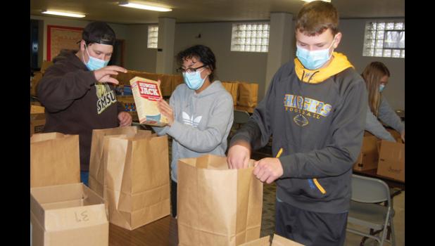 Mascot photo by Scott Thoma Left to right: Landon DeSmet, Chloe Davis, Sawyer DeSmet and Jeren Rost (background) were among the Area Mission Trip and National Honor Society students that packed 150 "Santa Bags" with food and beverages in the Hope Lutheran Church basement before distributing them to needy families in a drive-thru event at the Hope Lutheran parking lot last Thursday.