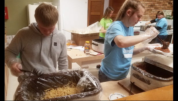 Photo by Nathan Schmig. Cole Myhre and Jeren Rost prepare take out meals in the Hope Lutheran Church basement.