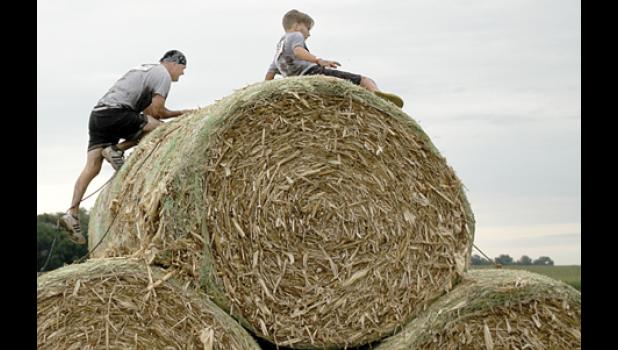 Staff photo by Scott Thoma. Minneota’s Seth Myhre climbed the bales with one other competitor just ahead of him during the “challenge” part of the mud run.