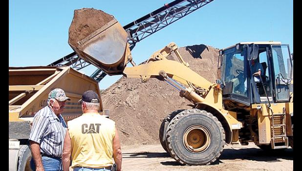 Staff photo by Scott Thoma. A worker digs into a pile of gravel at the pit as Bob Tolk talks to one of his drivers while another worker loads a truck. The rock wash plant located at the gravel pit.