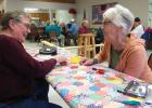 With several seniors playing card games in the background, Mary Ann Buysse, left and Rita Engels work on a quilt together at the Minneota Senior Center last week.